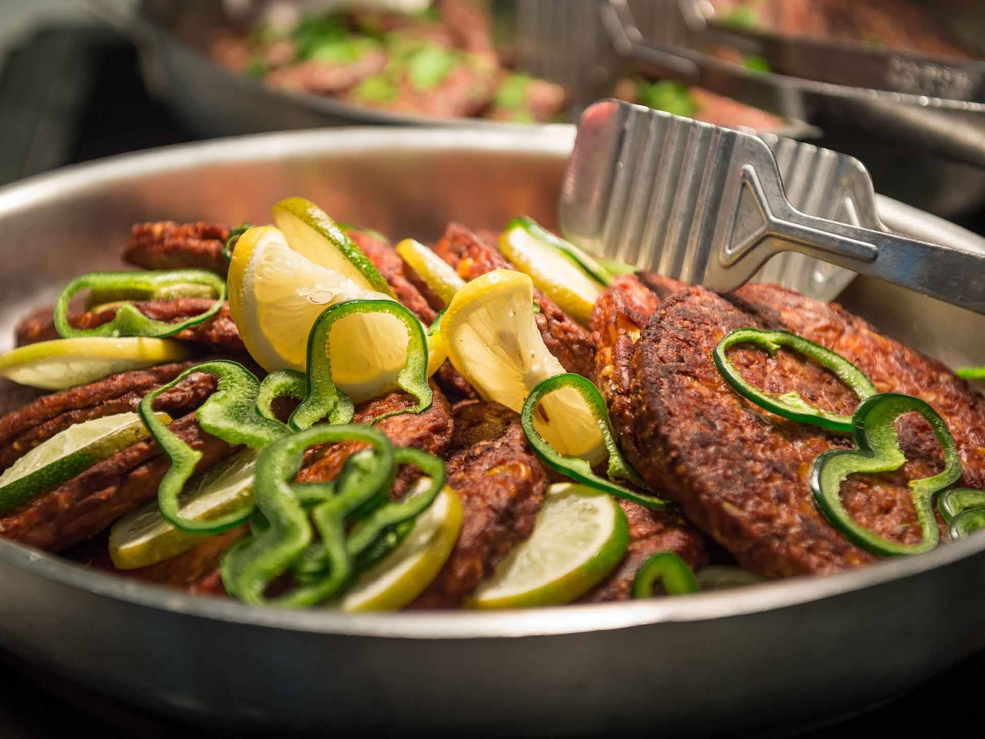 Saute pan and tongs with garden burgers, pepper, lime, and lemon slices
