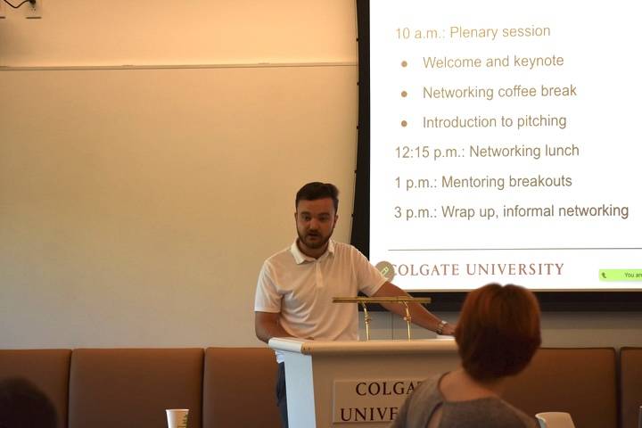 Man in white shirt standing in front of a screen addressing an audience 